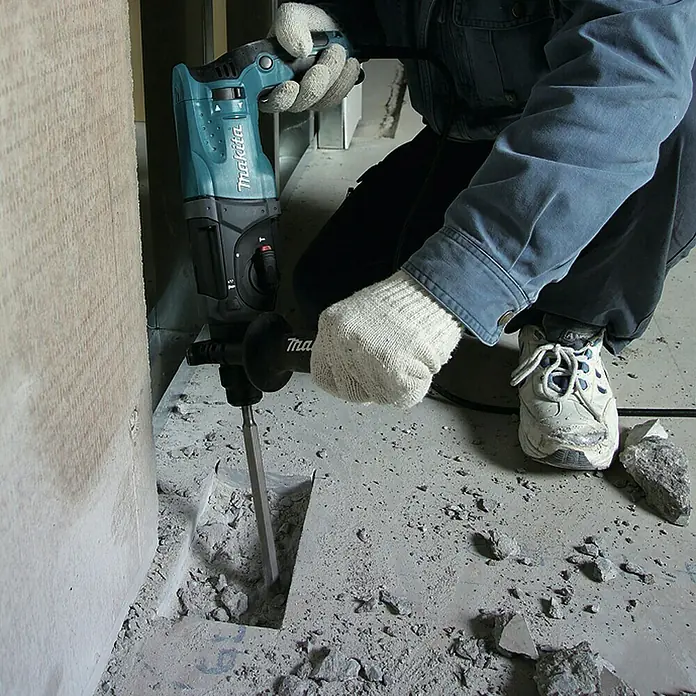 Makita Kombihammer HR2470 - 780 W, 2,7 J, SDS-Plus-Aufnahme - Türkis-schwarzer Makita Bohrhammer bricht Beton aus einem Boden, gehalten von einer Person mit Arbeitshandschuhen.