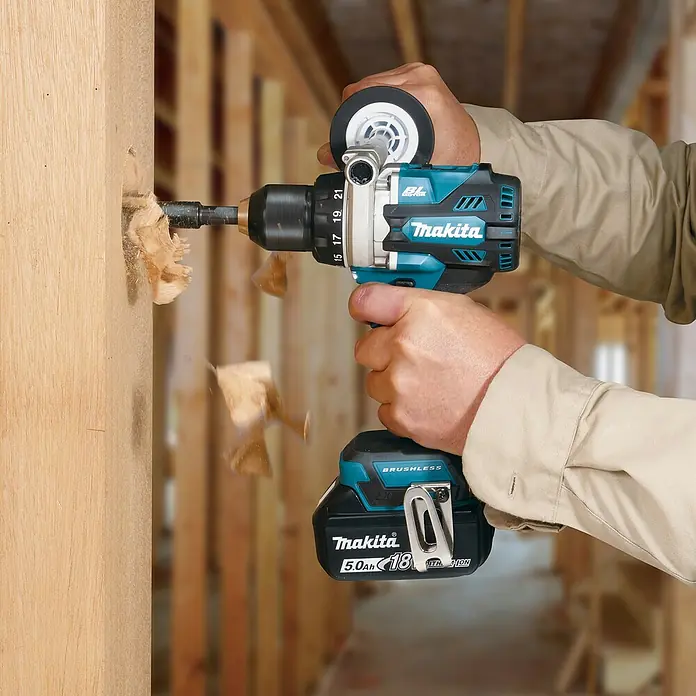 Makita LXT 18V Akku-Bohrschrauber DDF492RTJ - 18 V, 2 Akkus, 130 Nm - Eine Person benutzt eine türkise und schwarze Makita Akku-Bohrmaschine, um in einen Holzbalken zu bohren, wobei Holzspäne entstehen.