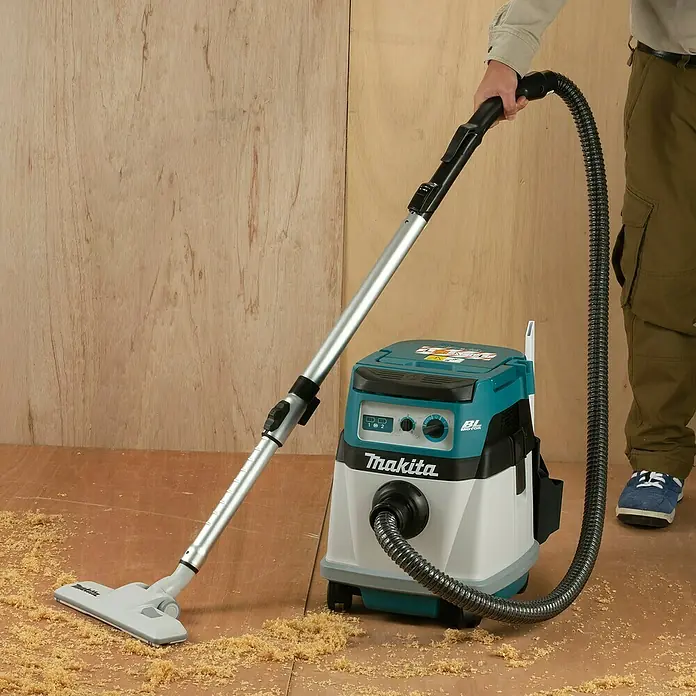 Makita LXT 18V Akku-Nass-Trockensauger DVC155LZX2 - 36 V, Ohne Akku, Behältervolumen: 15 l - Eine Person nutzt einen türkis-weißen Makita Staubsauger mit silberner Stange und schwarzem Schlauch, um Holzspäne von einem Holzboden zu saugen.
