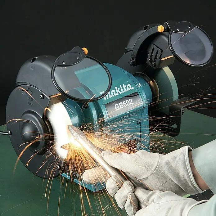 Makita Elektro-Doppelschleifer GB602 - 250 W, 2.850 U/min - Makita GB602 Schleifbock in Gebrauch, Funken fliegen, während eine behandschuhte Hand Metall schleift.