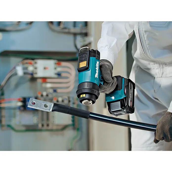 Makita XGT 40V max. Akku-Heißluftgebläse HG001G - 40 V, Ohne Akku, Temperaturbereich: 0 °C - 600 °C - Behandschuhte Hand verwendet Makita Akku-Heißluftpistole zum Schrumpfen einer Kabelklemme.