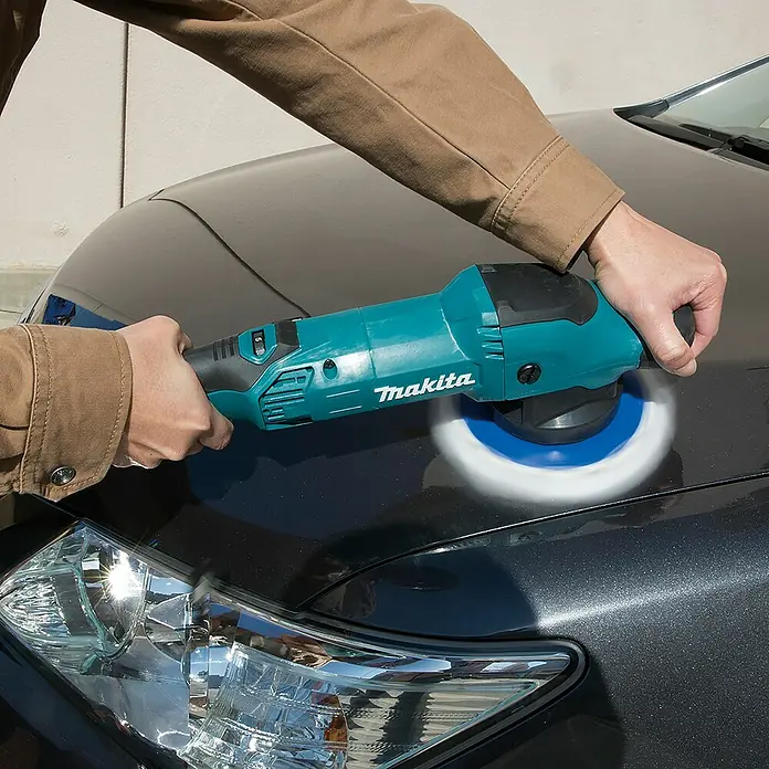 Makita Rotationspolierer PO5000C - 900 W, Durchmesser Scheibe: 125 mm - Person poliert eine dunkelgraue Motorhaube mit einem türkis-schwarzen Makita Polierer, wobei das weiß-blaue Polierpad in Aktion zu sehen ist.