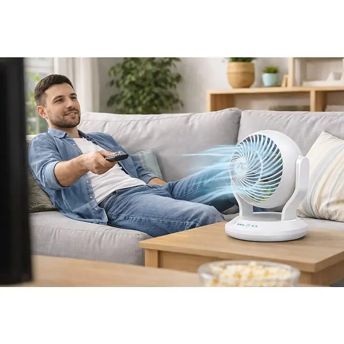 Arctic Air Tischventilator Gyro Cool - Weiß - Weißer, kugelförmiger Tischventilator auf einem Holztisch, der aktiv kühle Luft auf einen entspannten Mann auf der Couch bläst.