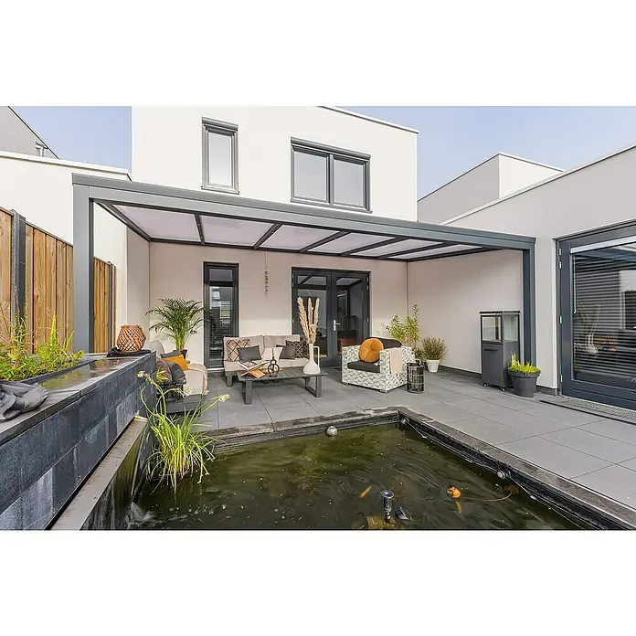 Gardendreams Terrassenüberdachung Essence - B x T: 500 x 335,5 cm, Anthrazitgrau, Verbundsicherheitsglas (VSG), Klar - Moderne Terrasse mit einer grauen Metallpergola, die einen Sitzbereich im Freien neben einem Teich beschattet, an einem weißen Haus.