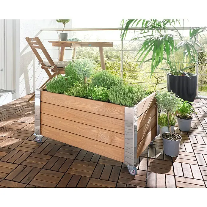 Dobar Hochbeet Rollfi - 78 x 52 x 40,5 cm, Holz, Braun - Pflanzkasten aus Holz auf Rollen mit Chrom-Akzenten, gefüllt mit Kräutern, auf einem Balkon.