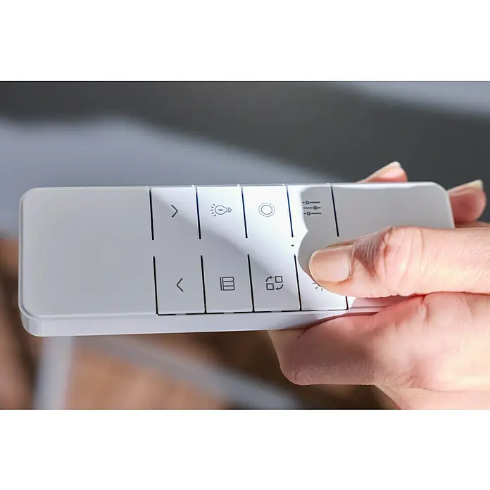 Sunfun LED-Vollkassettenmarkise - Anthrazit, Breite: 3 m, Ausfall: 2 m - Eine Hand hält eine weiße Fernbedienung mit verschiedenen Licht- und Einstellungssymbolen auf den Tasten.