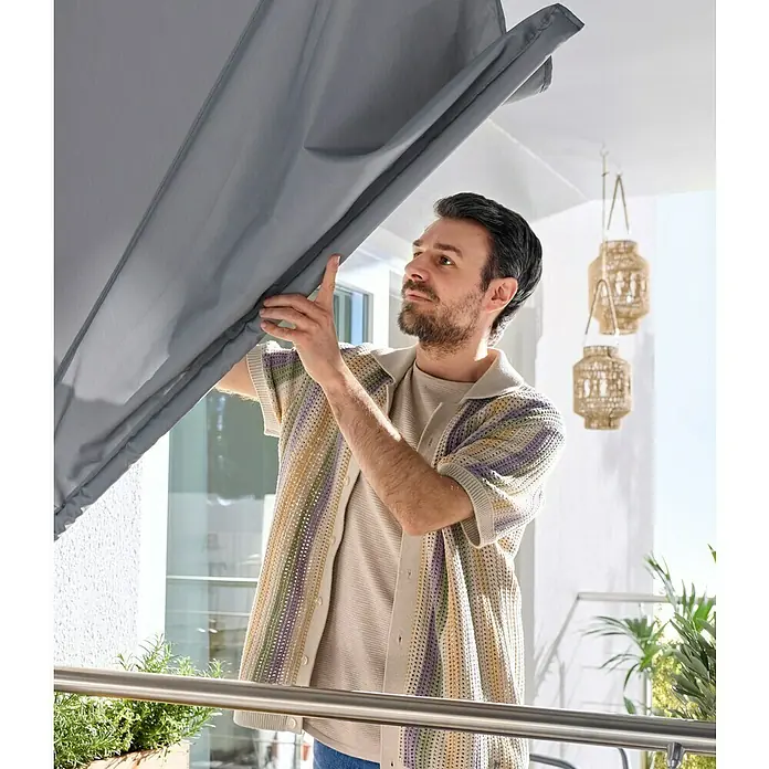 Sunfun Balkonfächer - Grau, 1,4 x 1,4 m - Mann auf einem Balkon passt eine graue Stoffmarkise an.
