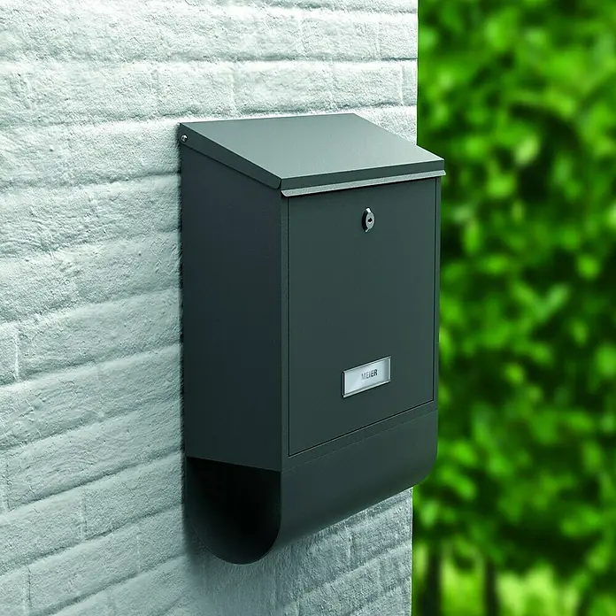 Basi Wandbriefkasten BK 300 M - L x B x H: 11,8 x 30,1 x 38,6 cm, Anthrazit, Stahl, Zeitungsfach - Dunkelgrauer Metallbriefkasten mit schrägem Deckel und Namensschild 'MEIER', montiert an einer weißen Ziegelwand.