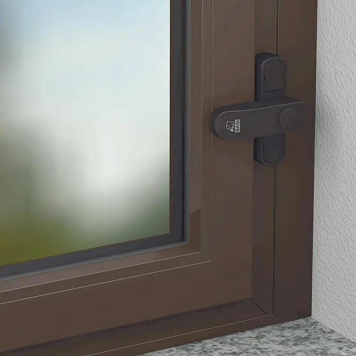 Basi Fenstersicherung FS 500 - Einflügelig, Braun - Brauner Fensterrahmen mit dunkelgrauem Sicherheitsgriff mit BASI-Logo.