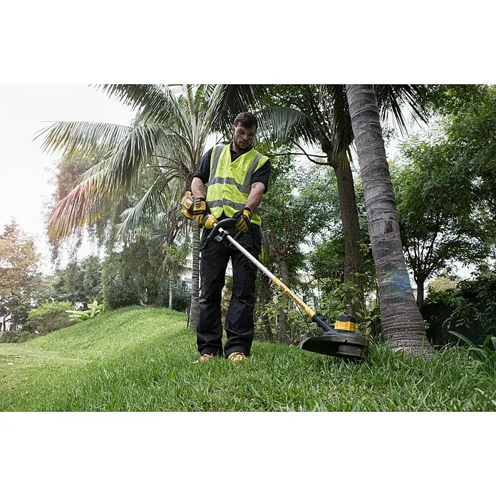 DeWalt XR 18V Akku-Rasentrimmer DCM561PBS-XJ - Ohne Akku, Schnittbreite Faden: 33 cm - Ein Mann in Warnweste und Schutzbrille mäht mit einem gelb-schwarzen Rasentrimmer Gras in einem Garten.