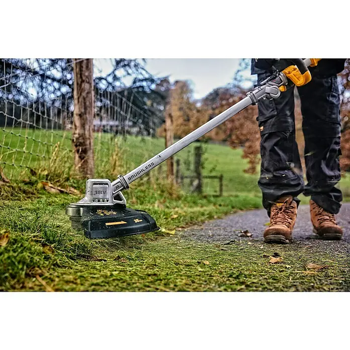 DeWalt XR 18V Akku-Rasentrimmer DCMST561N-XJ - 18 V, Ohne Akku, Schnittbreite Faden: 36 cm - Kabelloser, grau-schwarzer Rasentrimmer in Gebrauch, von einer Person in Arbeitsstiefeln zum Grasschneiden am Wegrand gehalten.