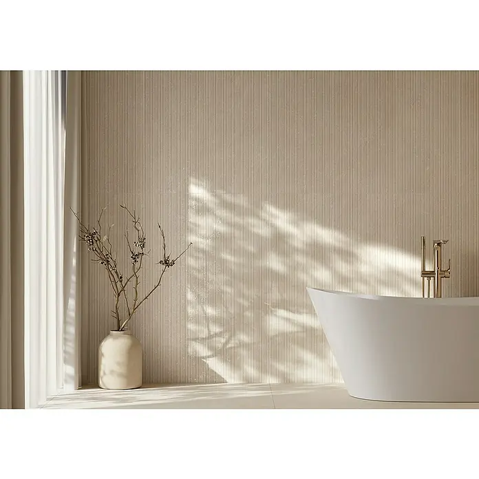 Wandfliese Manresa Lines - 39,8 x 119,8 cm, Beige, Matt - Modernes Badezimmer mit einer weißen freistehenden Badewanne und goldener Armatur. Sonnenlicht beleuchtet die beigefarbenen Wände.