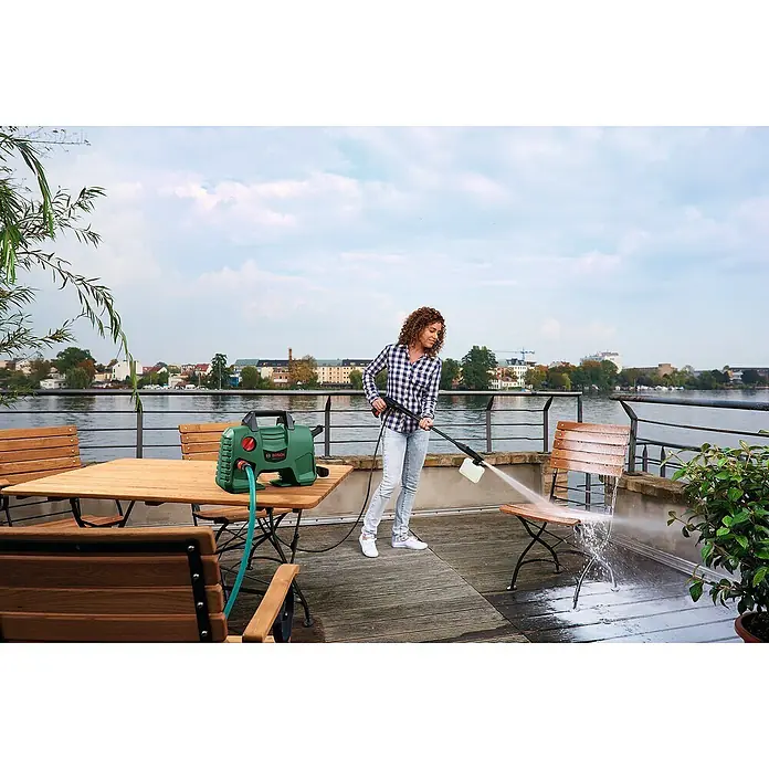 Bosch Hochdruckreiniger EasyAquatak 110 - 1.300 W, Max. Druck: 110 bar, Fördermenge: 330 l/h - Eine Frau reinigt einen Holzstuhl auf einem Deck mit einem grünen Bosch Hochdruckreiniger, der effiziente Terrassenmöbelreinigung zeigt.