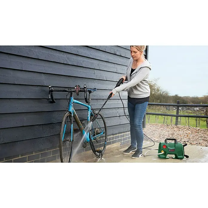 Bosch Hochdruckreiniger EasyAquatak 110 - 1.300 W, Max. Druck: 110 bar, Fördermenge: 330 l/h - Frau reinigt ein blaues Fahrrad mit einem grün-schwarzen Hochdruckreiniger.