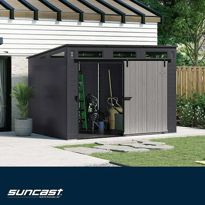 Suncast Gerätehaus - Kunststoff - Dunkelgraues Gerätehaus aus Kunststoff mit hellgrauer Schiebetür in Holzoptik, offen im Garten mit Gartengeräten.
