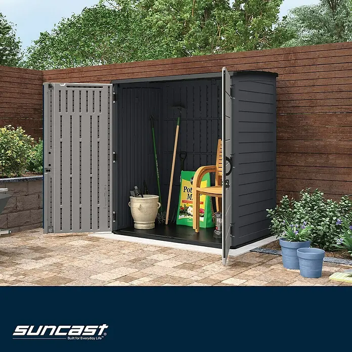 Suncast Geräteschrank - Kunststoff - Zweifarbiger Suncast Geräteschuppen, offen mit Gartengeräten und Blumenerde auf einer Terrasse.