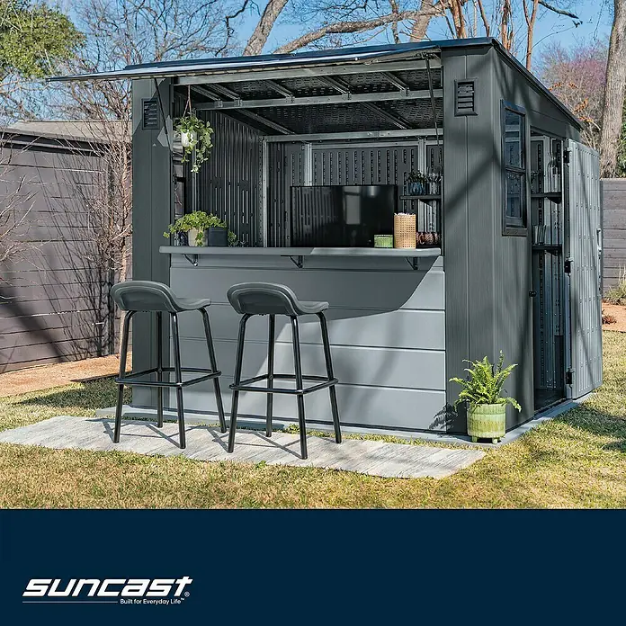 Suncast Gartenhaus Cabana - L x B x H: 250 x 222 x 226 cm, Kunststoff - Grauer Outdoor-Schuppen aus Harz, als Außenbar mit zwei Hockern auf einem Rasen genutzt.