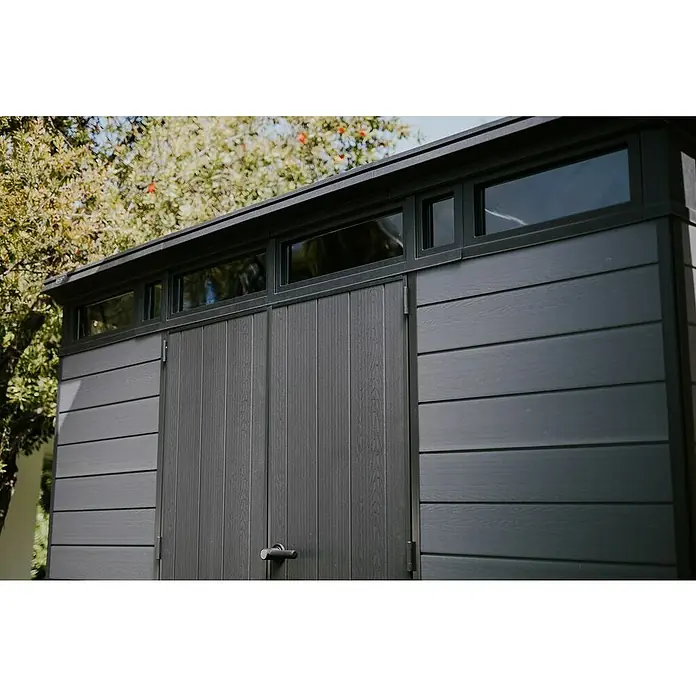 Keter Caseta de jardín Cortina 11x7 - Medidas ext. (An x Pr): 342 x 218 cm, Plástico, Gris, 7,4 m² - Caseta de jardín gris oscuro con revestimiento de madera, puertas dobles y ventanas superiores, al aire libre entre árboles.