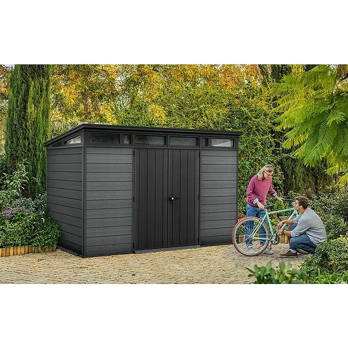 Keter Caseta de jardín Cortina 11x7 - Medidas ext. (An x Pr): 342 x 218 cm, Plástico, Gris, 7,4 m² - Cobertizo de jardín gris oscuro de composite con puertas dobles y ventanas superiores. Una pareja con bicicleta muestra su tamaño y función.