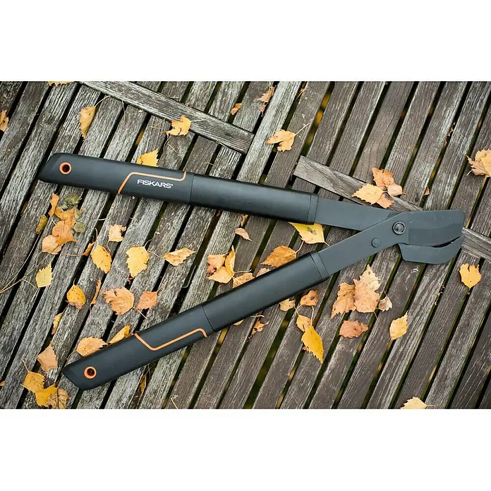 Fiskars SingleStep Hand-Astschere L28 - Länge: 57 cm, Max. Aststärke: 35 mm, Stahl, Schwarz/Orange - Eine schwarze Fiskars Astschere liegt auf einem Holztisch, umgeben von Herbstlaub. Ideal für die Gartenarbeit.
