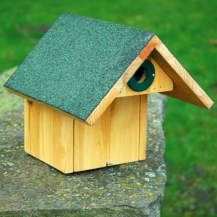 Dobar Nistkasten Räuberschutz - 25,5 x 29 x 25,5 cm, Natur/Grün, Holz - Ein hölzernes Vogelhaus mit einem grünen Dach und einem runden Eingang auf einem Stein. Ideal für Gartenliebhaber und Vogelfreunde.