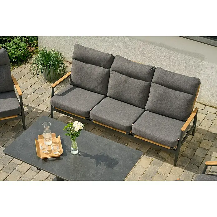 Siena Garden Roma Loungemöbel-Set - 3 -tlg., Grau, Aluminium - Graues Outdoor-Sofa-Set mit Holzarmlehnen und geflochtenen Details, auf einer gepflasterten Terrasse mit einem dunklen Tisch und einer Pflanze.