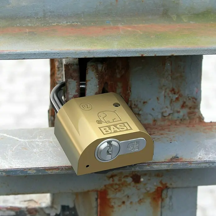 Basi Vorhangschloss VHS PZ - B x H: 28 x 46,5 mm, Bügelinnenhöhe: 40 mm, Material Bügel: Gehärteter Spezialstahl - Goldenes Messingschloss sichert ein verwittertes, rostiges Metalltor.