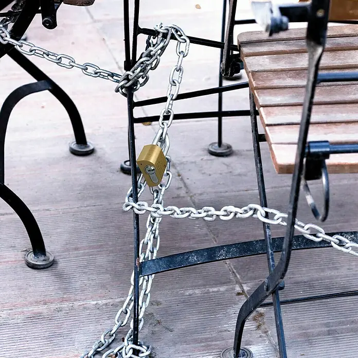 Basi Vorhangschloss VHS PZ - B x H: 28 x 46,5 mm, Bügelinnenhöhe: 80 mm, Material Bügel: Gehärteter Spezialstahl - Messingschloss und Metallkette sichern Outdoor-Stühle auf einer Holzterrasse.