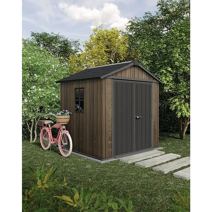 Keter Caseta de jardín Apex 757-775 - Medidas ext. (An x Pr): 223 x 230 cm, Plástico, Nogal/Negro - Un cobertizo de jardín marrón con apariencia de madera, puertas y techo gris oscuro, en un jardín junto a una bicicleta rosa.