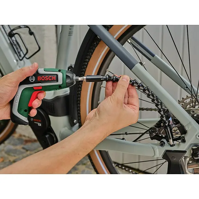 Bosch Akkuschrauber IXO 7 - 3,6 V, 1 Akku, 2 Ah, 5,5 Nm, Flexi-Set - Hände verwenden einen grün-schwarzen Bosch IXO Akkuschrauber mit flexiblem Bit-Halter, um eine Schraube am Hinterrad eines Fahrrads festzuziehen.