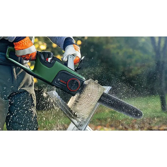 Bosch Sägekette - Länge: 35 cm, Schnittlänge: 35 cm, Passend für: Bosch Kettensäge AKE 35, 35-17 und 35-18 - Grüne und schwarze Bosch Kettensäge sägt einen Holzbalken, Sägespäne fliegen. Eine Person hält die Säge mit Handschuhen.