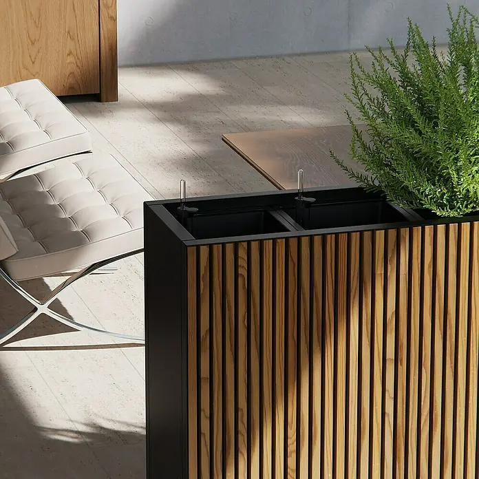 Herstera Garden Pflanzkasten Deco Planter - Außenmaß (L x B x H): 120 x 40 x 80 cm, Holz, Braun/Schwarz - Selbstbewässernder Pflanzkübel mit Holzlatten und schwarzem Rahmen, mit Grünpflanzen, neben einer gepolsterten Bank.