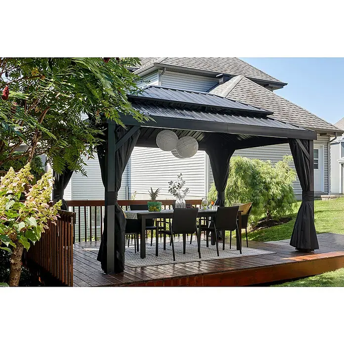 Sojag Standard-Pavillon London 1014 - L x B x H: 424,3 x 299,3 x 310 cm, Aluminium, Schwarz - Dunkler Metallpavillon mit Wellblechdach und schwarzen Sichtschutzvorhängen, spendet Schatten für einen Essbereich im Freien auf einer Holzterrasse.