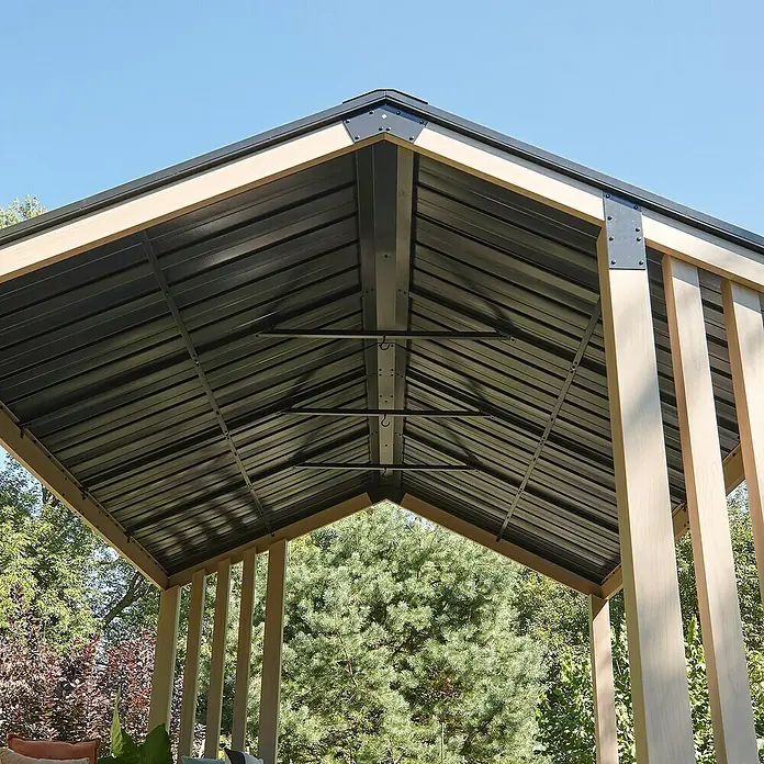 Sojag Standard-Pavillon Lito 1012 - L x B x H: 368,4 x 298 x 296 cm, Natur/Schwarz, Aluminium - Blick von unten auf ein Pavillondach mit dunklen Wellblechpaneelen, hellbraunem Holzrahmen und dunklen Metallverbindern, vor blauem Himmel und Bäumen.