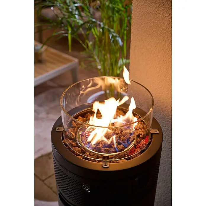 Kingstone Feuerstelle Sunset - Ø x H: 38 x 99 cm, Schwarz, Leistung: 5 kW - 9 kW - Ein Outdoor-Feuerstellenheizer mit dunklem Metallsockel, Glaszylinder und Lavasteinen, mit hellen Flammen auf einer Terrasse.