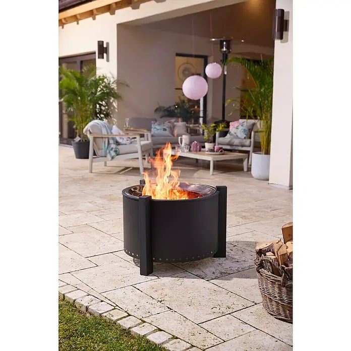 Kingstone Feuerschale Clear Flame - Durchmesser: 70 cm, Stahl - Ein schwarzer Metall-Feuertisch mit brennenden Flammen, der Wärme auf einer Terrasse mit stilvollen Möbeln spendet.