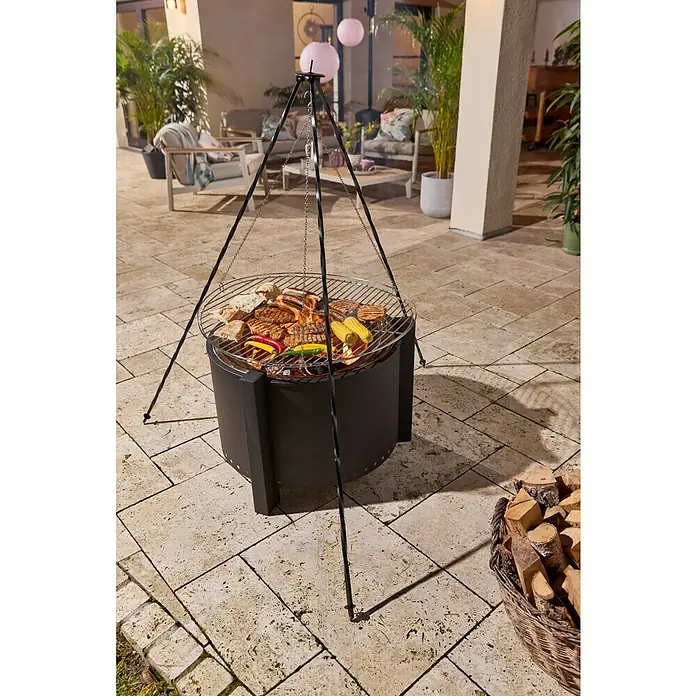 Buschbeck Trébede Parrilla colgante - Diámetro: 60 cm - Barbacoa de metal negro con parrilla de trípode, cocinando carne, pan y verduras en un patio.