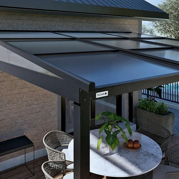 Sojag Terrassenüberdachung Budavar - Schwarz, Metall, L x B x H: 298,5 x 366,5 x 243 cm - Dunkle moderne Terrassenüberdachung mit transluzentem Dach über einem Essbereich im Freien an einem Ziegelhaus.
