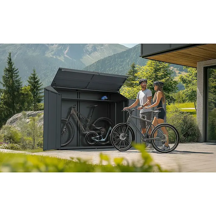 Westmann Fahrradgarage Linea - Anthrazit - Dunkelgraue Metall-Fahrradbox, geöffnet, mit Fahrrädern darin, neben zwei Radfahrern mit ihren Rädern in einer Berglandschaft.