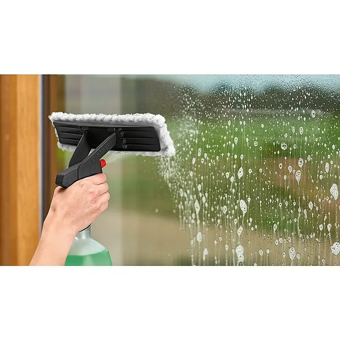Akku-Fenstersauger - 3,6 V, 2 Ah, Behältervolumen: 100 ml - Eine Hand hält eine schwarze Bosch Fensterreiniger-Sprühflasche mit weißem Pad und sprüht Flüssigkeit auf ein schäumendes Fenster.