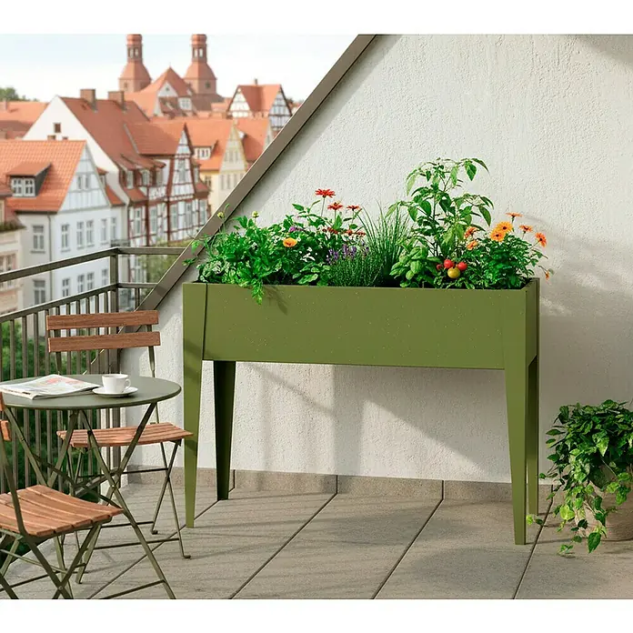 Westmann Hochbeet Vedura - 30 x 100 x 80 cm, Metall, Olivgrün - Grünes Hochbeet auf einem Balkon, gefüllt mit verschiedenen Pflanzen, neben einem kleinen Tisch und Stühlen.