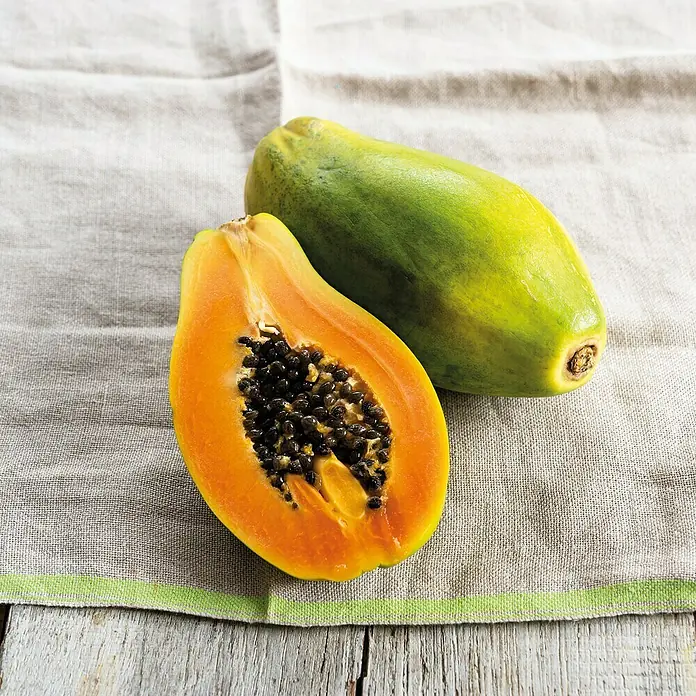 Piardino Papaya - Carica papaya, Topfgröße: 13 cm - Zwei Papayas, eine ganze grün-gelb, eine geschnittene orange Hälfte mit schwarzen Kernen.