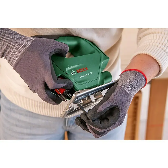 Bosch Power for All 18V Maschinen-Set 2-Tool-Kit EasyImpact + EasySaw - 18 V, 2 Akkus, 2 Ah, 5 -tlg. - Person mit Handschuhen hält eine grüne Bosch EasySaw 18V-70 Stichsäge und justiert das Sägeblatt.