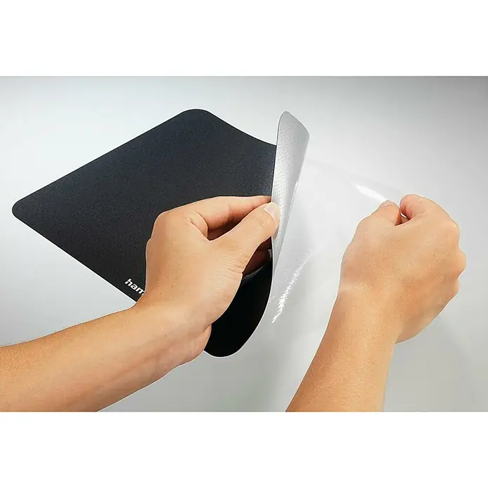 Hama Unterlage Laser-Mauspad 126865 - Schwarz, 18 x 22 cm - Eine Person zieht eine schwarze Mausmatte von ihrer Schutzfolie ab, die die gepunktete Klebefläche zeigt.
