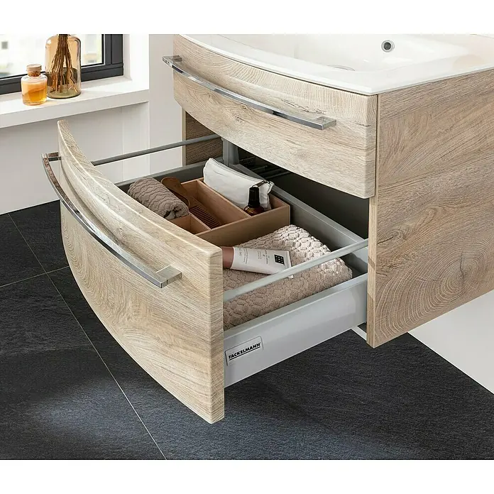Fackelmann B.style Badmöbel-Set - Gesamtbreite Badmöbel: 63,2 cm, Nature Oak Holzoptik - Badezimmerschrank in heller Holzoptik mit geöffneter Schublade, die organisierte Toilettenartikel und Handtücher zeigt.