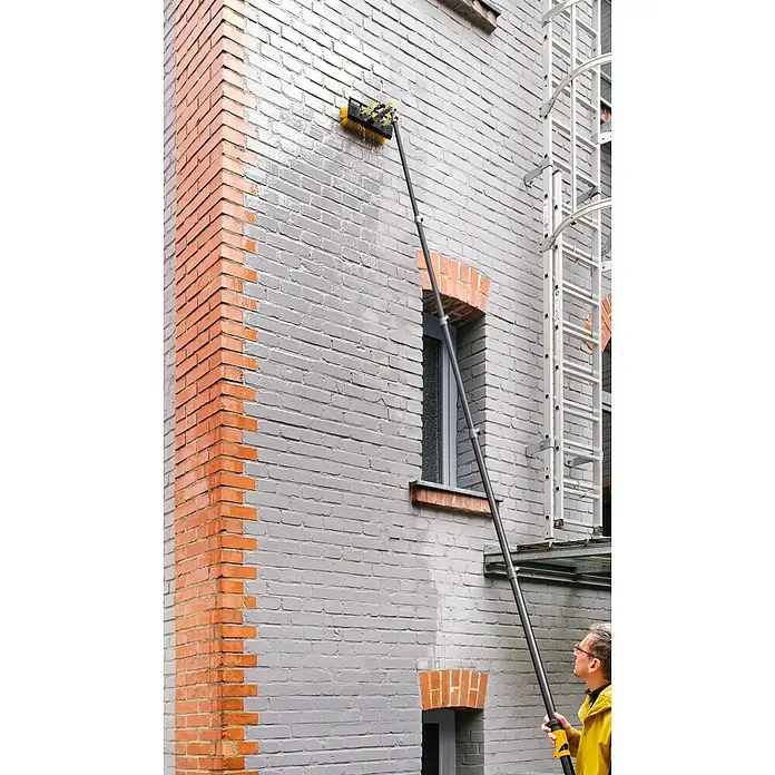 Neptun PV-  & Fassaden Reinigungsset mit verschiedenen Aufsätzen - Teleskopstiel, 120 cm - 490 cm - Eine Person reinigt eine graue Ziegelwand mit einer langen, schwarz-gelben Bürste mit Wasserstrahl.