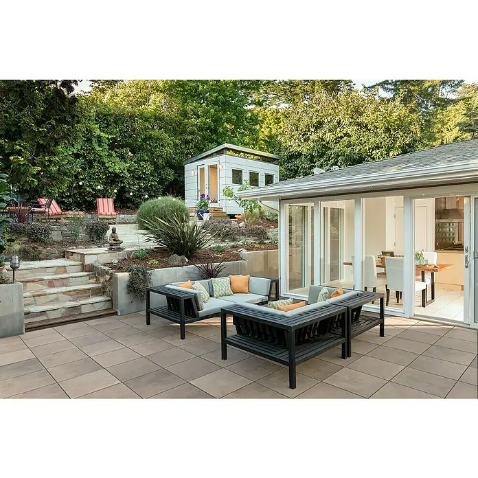EHL Terrassenplatte Design - 60 x 60 x 4 cm, Braun-Beige, Beton - Braune quadratische Terrassenplatten bilden einen Außenbereich mit Sitzgelegenheiten neben einem Haus.