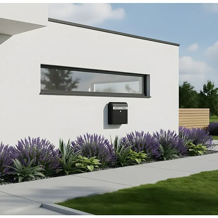 Allux Briefkasten KS200 - L x B x H: 170 x 400 x 445 mm, Schwarz, Stahl, Namensschild - Schwarzer Briefkasten an weißer Hauswand, umgeben von lila Lavendel und einem Betonweg.