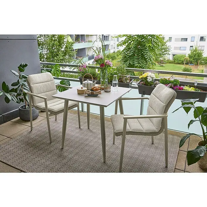 Sunfun Solo Balkontisch - L x B x H: 74 x 74 x 74 cm, Aluminium, Sintered Stone, Quadratisch, Light-Greige - Ein hellgraues Outdoor-Essset mit zwei gepolsterten Stühlen und einem gemusterten Teppich auf einem Balkon, für eine Mahlzeit arrangiert.