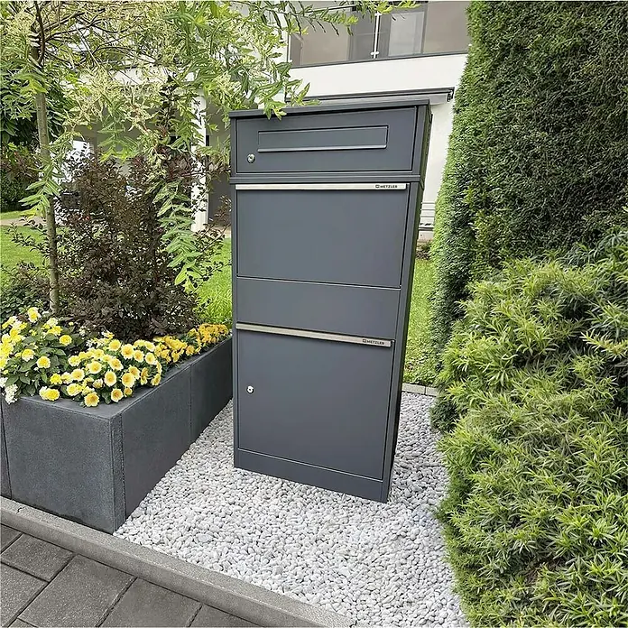 Metzler Paketbox Bispo - L x B x H: 37,3 x 50,2 x 112 cm, Anthrazit, Stahl, Paketfach - Dunkelgrauer, mehrfächeriger Paketbriefkasten von METZLER, auf weißem Kies in einem Garten stehend.